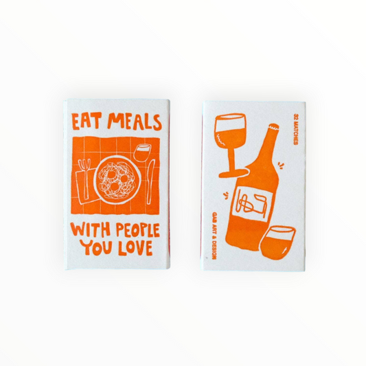 Two small rectangular cards or boxes on a white background, each printed with orange food-and-drink illustrations and text. The left one reads “EAT MEALS WITH PEOPLE YOU LOVE” and shows a plate, fork, knife, and drink.
