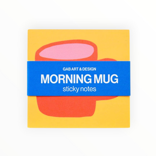 A square sticky note pad with a bright yellow background, a pink and orange abstract mug illustration, and a blue paper band across the center reading 'GAB ART & DESIGN MORNING MUG sticky notes'.