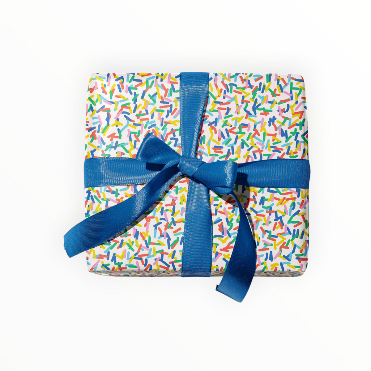 A square gift box wrapped in white paper covered with a multicolor sprinkle pattern, tied with a royal blue satin ribbon and bow, on a solid white background.
